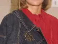 Eine Frau trägt eine rote Bluse und eine blaue Jeansjacke mit einer goldenen Schmetterlingsbrosche.