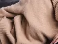 Eine Frau in einem beigen Kaschmirpullover liegt entspannt auf einem dunklen Sofa. Das Kaschmir waschen ist wichtig für die Pflege.