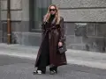 Frau in braunem Leder-Trenchcoat und schwarzen Hosen. Die Frage, welche Farbe passt zu schwarz, wird hier elegant beantwortet: Braun und Schwarz sind ein tolles Duo.