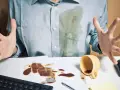 Mann mit verschüttetem Kaffee auf Hemd und Schreibtisch. Eingetrocknete Kaffeeflecken entfernen ist eine Herausforderung.