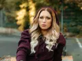 Frau mit blonden Haaren und Brille trägt einen Kapuzenpullover in dunklem Beere. Die Farbe Beere kombiniert sie gekonnt mit ihrem Outfit.