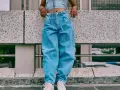 Person in einem lässigen baggy jeans outfit mit Crop-Top und weißen Sneakern steht auf einer Betonmauer.