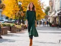 Frau spaziert lächelnd in einer grünen Tunika mit Leggings und braunen Stiefeln durch eine herbstliche Stadt.