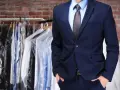 Mann im Anzug vor Kleiderständer mit frisch gereinigter Kleidung. Professionelle Anzug Reinigung für makellose Auftritte.
