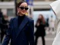Eine Frau mit Sonnenbrille und auffälligem Schmuck trägt einen dunkelblauen Blazer über einem schwarzen Rollkragenpullover. Sie kombiniert dunkelblau und schwarz gekonnt.