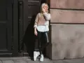 Eine Frau kombiniert elegant schwarze Hose mit einem zweifarbigen Pullover und weißem Hemd. Weiße Plateau-Sneaker runden den Look ab.
