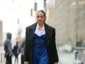 Frau trägt eine schwarze Jacke über einem blauen Nadelstreifen-Jumpsuit mit Korsett-Oberteil und weißem Hemd.