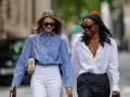 Zwei Frauen in lässiger Kleidung, eine mit blau-weiß gestreifter Bluse und weißer Hose, die andere mit weißer Bluse und dunkler Hose.