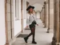 Frau mit Hut und gestreiftem Pullover, die stylische ledershorts kombinieren. Schwarze Stiefel und Strumpfhose runden den Look ab.