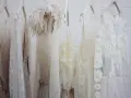 Mehrere zarte, weiße Brautkleider hängen an Kleiderbügeln. Eines hat eine Federverzierung. Die Reinigung eines Hochzeitskleides ist wichtig, damit es schön bleibt.