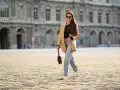 Frau in weiter Jeans und blauem Hemd mit goldener Clutch und Glitzer-Schuhen überquert Straße.