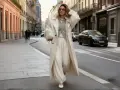 Frau in beigem Trenchcoat und weiten Hosen, minimalistischer Stil, geht auf einer Straße in einer europäischen Stadt.