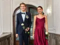 Elegantes Outfit für einen Jugendweihe Gast: Ein junger Mann im dunkelblauen Anzug mit Fliege und eine Frau im weinroten Kleid.