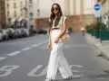 Stilvolle Dame in Paris, die eine weiße Leinenhose kombiniert mit einem kurzen Top und einer Umhängetasche trägt.