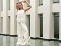 Frau in weißem Outfit mit weiten Palazzo Hosen, elegant gestylt vor moderner Architektur.