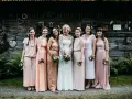 Brautjungfern in zarten Pastelltönen posieren vor rustikaler Holzwand, ein Bild von einer entspannten boho hochzeit.