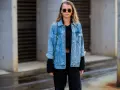 Stylische Frau mit lässiger Jeansjacke kombinieren mit schwarzem Crop-Top und Hose. Sonnenbrille und kleine Tasche runden den Look ab.