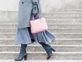 Stilvoll **Kleider im Winter tragen**: Grauer Mantel, blauer Rock, schwarze Stiefel und eine rosafarbene Tasche auf Steinstufen.