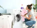 Junge Frau lädt Wäsche in die Waschmaschine. Sie hält ein rosa gestreiftes Kleidungsstück, bereit zum leinen waschen.