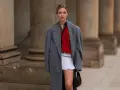 Ein junges Model präsentiert einen preppy look mit grauem Mantel, rotem Pullover und weißem Faltenrock.
