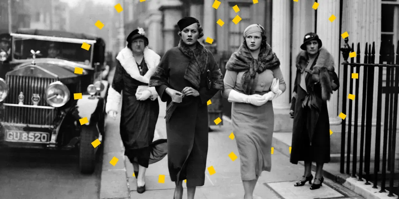 Vier Frauen in eleganter 30er Jahre Mode, Pelzmänteln und Hüten spazieren an einem Oldtimer entlang.