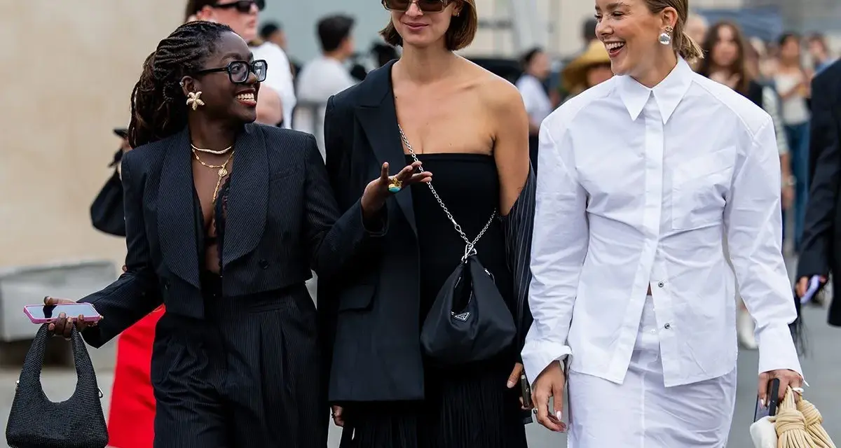 Drei Frauen präsentieren unterschiedliche, modische clothing styles: ein schwarzer Anzug, ein schwarzes Kleid mit Fransen und ein weißes Hemd mit Rock.