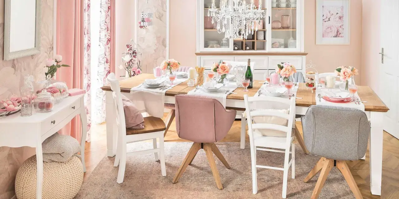 Ein Esstisch im Cottagecore-Stil, gedeckt mit Blumen und rosafarbenen Akzenten. Ein Kronleuchter hängt über dem Tisch.