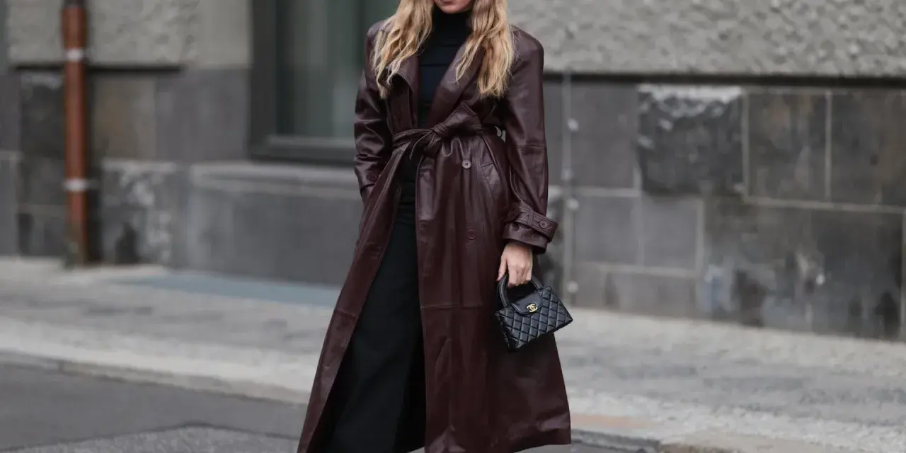 Frau in braunem Leder-Trenchcoat und schwarzen Hosen. Die Frage, welche Farbe passt zu schwarz, wird hier elegant beantwortet: Braun und Schwarz sind ein tolles Duo.