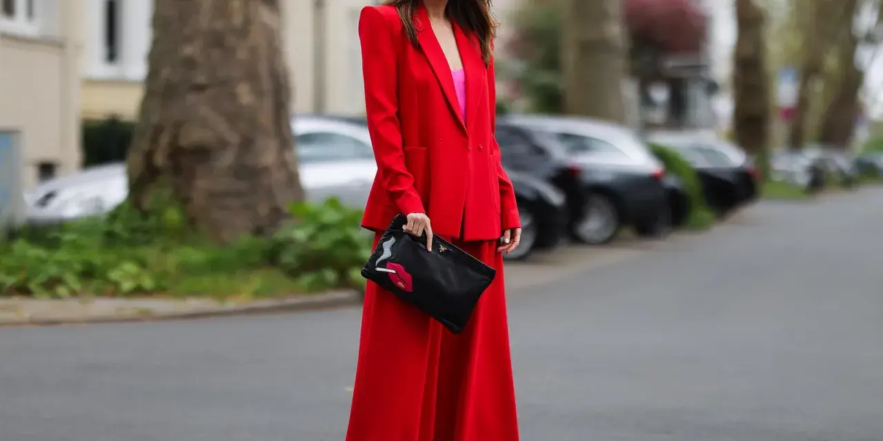 Frau in rotem Hosenanzug mit pinkem Top und Clutch mit Lippenmotiv. Was passt zu roter Hose? Dieser Look zeigt es!
