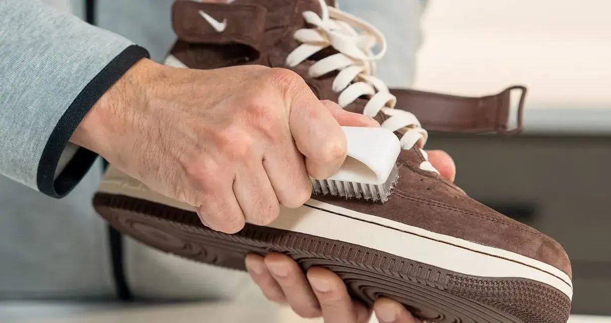 Hände reinigen braune Wildleder Schuhe mit einer Bürste. So werden die Lieblingssneaker wieder wie neu.