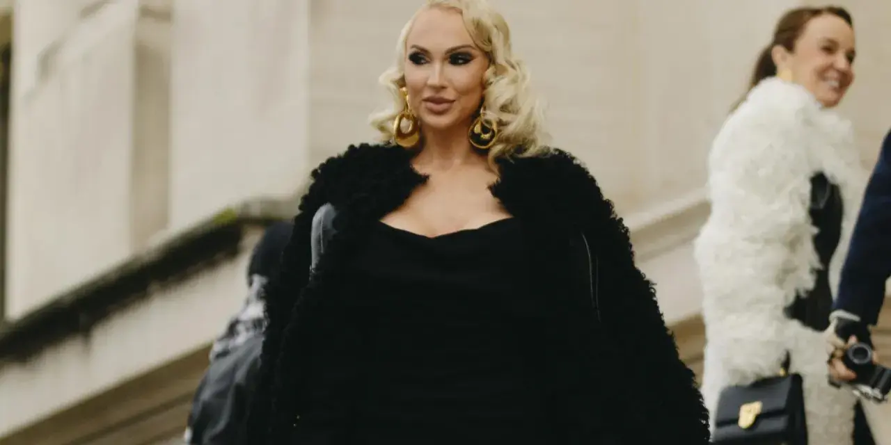 Eine Frau im Stil einer "mob wife" mit blonden Locken, großen goldenen Ohrringen und einem schwarzen Pelzmantel.