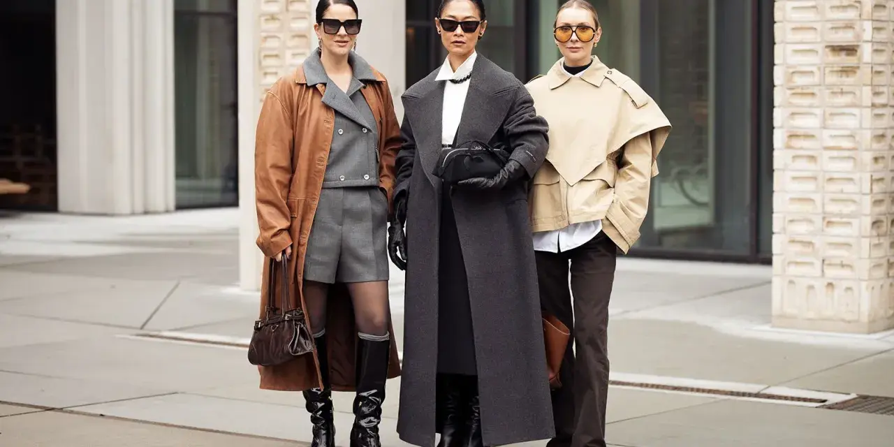 Drei Frauen präsentieren stilvolle Outfits im layering look: brauner Mantel über grauem Anzug, langer grauer Mantel und beiger Kurzmantel über weißem Hemd.