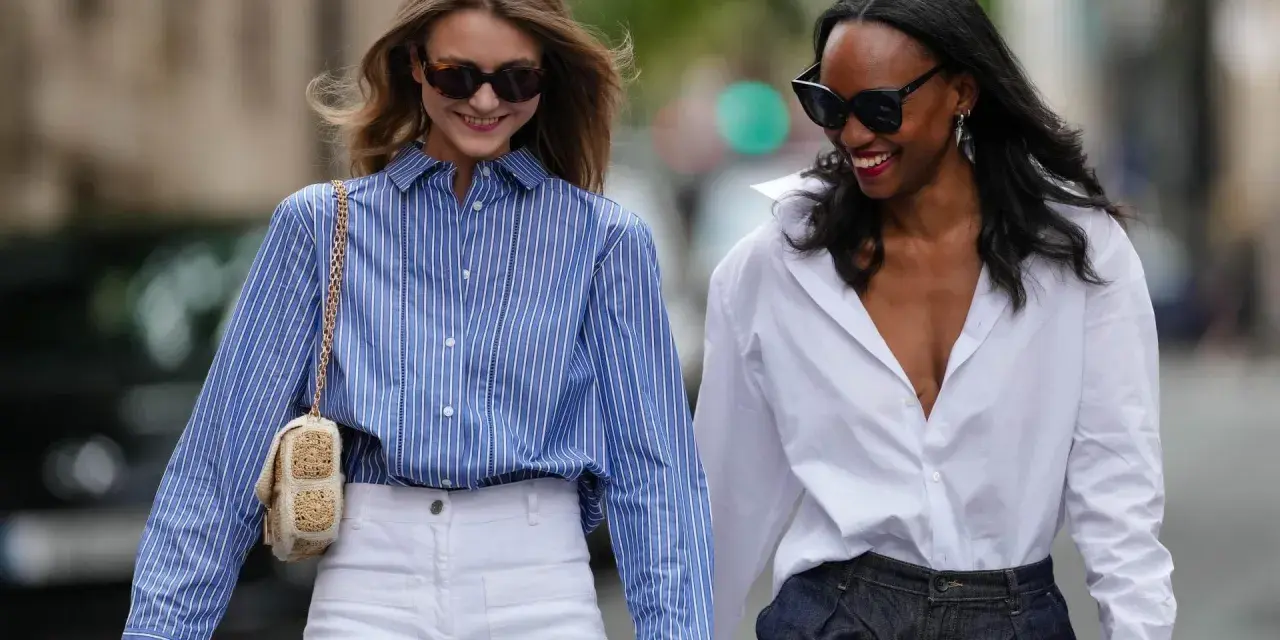 Zwei Frauen in lässiger Kleidung, eine mit blau-weiß gestreifter Bluse und weißer Hose, die andere mit weißer Bluse und dunkler Hose.