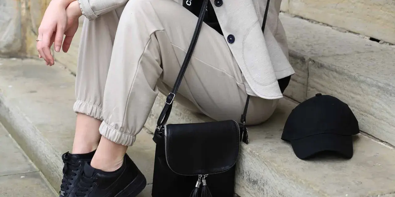 Stylisches flugzeug outfit damen: beige Hose, Blazer, schwarze Sneaker, Tasche und Cap. Perfekt für die Reise.