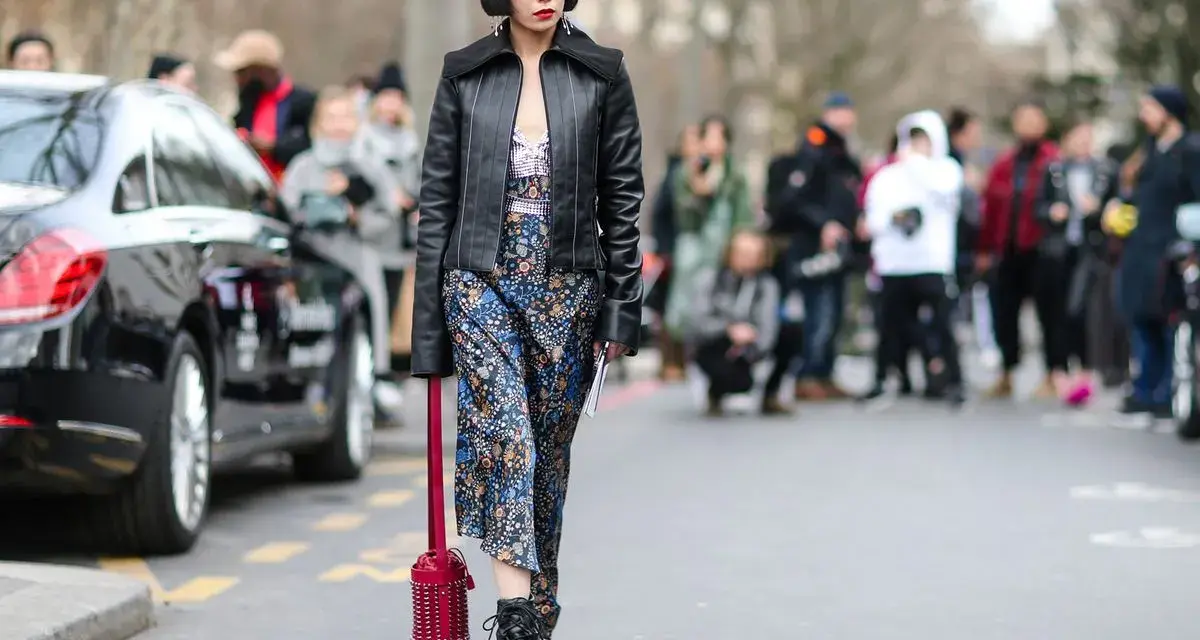 Frau im typisch 90er Grunge Style mit Lederjacke, geblümtem Kleid und Stiefeln. Ein roter Nietenbeutel rundet den Look ab.