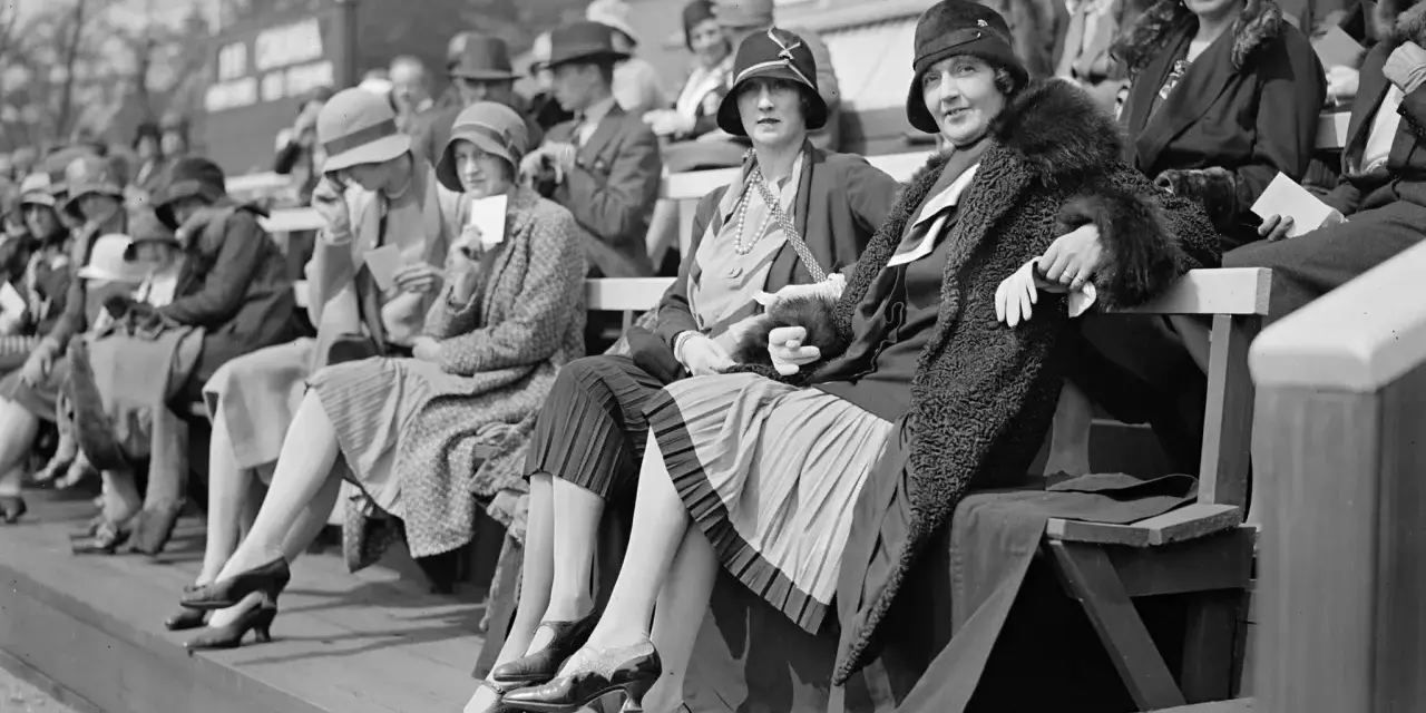 Frauen in eleganten Hüten und Kleidern, ein Bild der Weimarer Republik Mode, sitzen auf einer Tribüne.