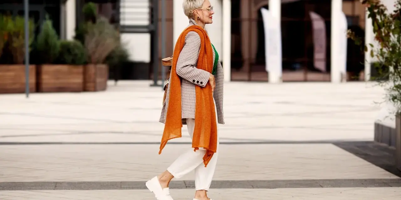 Coole Frauen mit 50: Stilvoll in kariertem Blazer, orangefarbenem Schal und weißen Hosen.