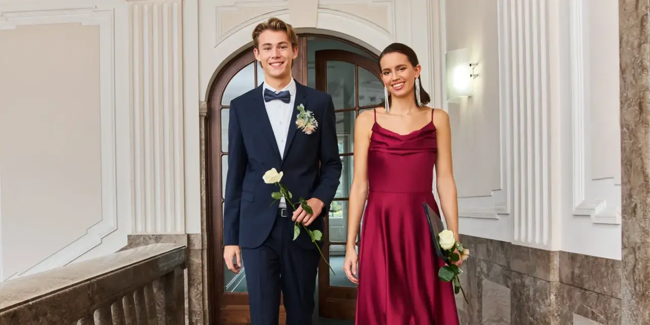 Elegantes Outfit für einen Jugendweihe Gast: Ein junger Mann im dunkelblauen Anzug mit Fliege und eine Frau im weinroten Kleid.