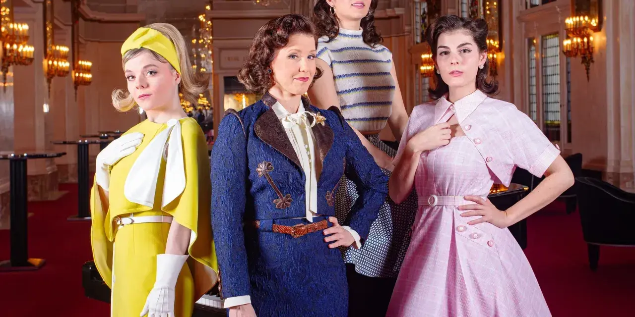 Vier Frauen in stilvollen Outfits, die an die Kleiderordnung des Theater des Westens erinnern, posieren vor einem opulenten Hintergrund.