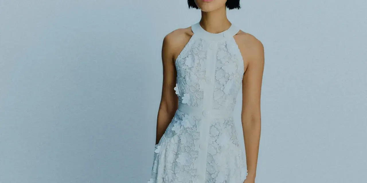 Ein Model trägt ein weißes Spitzenkleid mit Blumenapplikationen. Welche Farbe passt zu Himmelblau? Dieses Kleid ist eine zarte Antwort.