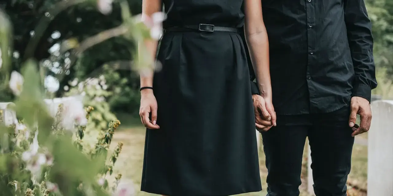 Frau in schwarzem Kleid und Mann in schwarzer Kleidung halten Händchen. So zieht man zur Beerdigung an als Frau.
