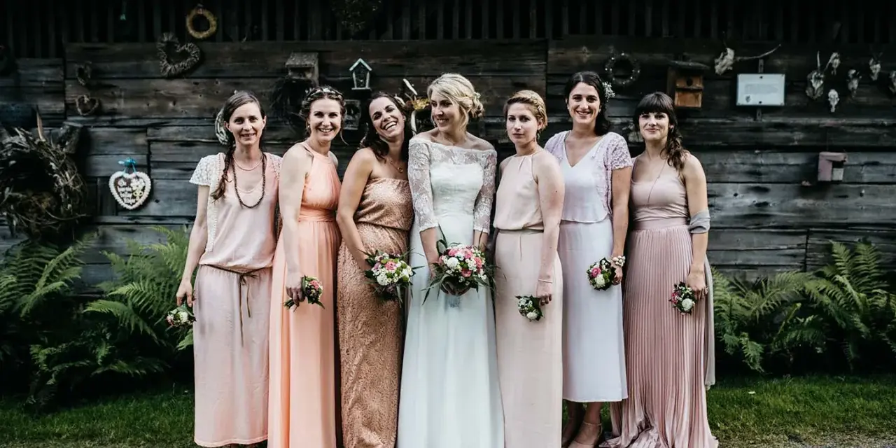 Brautjungfern in zarten Pastelltönen posieren vor rustikaler Holzwand, ein Bild von einer entspannten boho hochzeit.