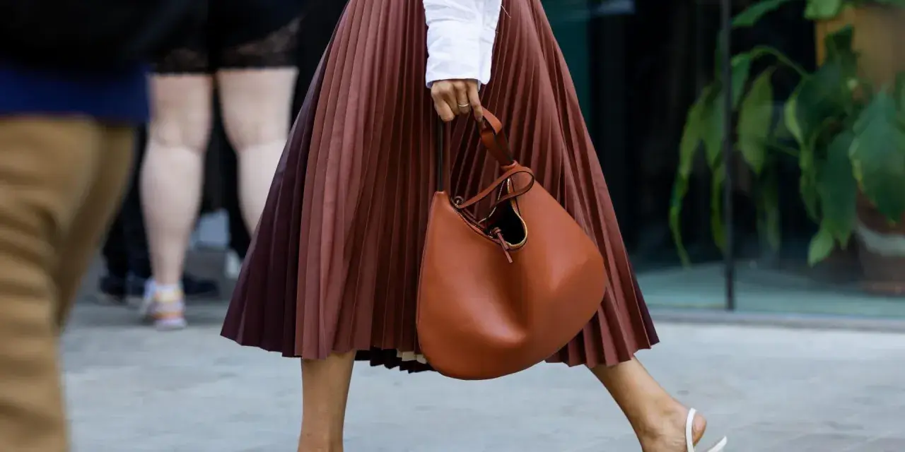 Elegant brauner Faltenrock, kombiniert mit weißer Bluse und cognacfarbener Tasche. Ein stilvoller Look für den Sommer.