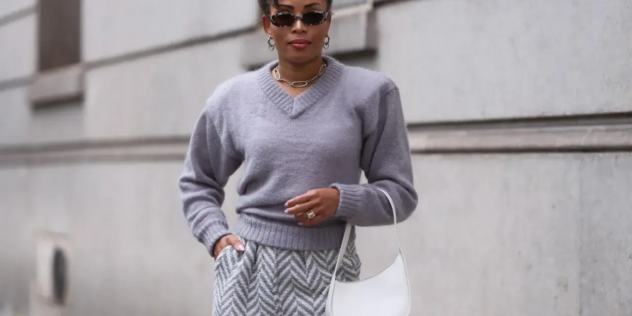 Eine Frau in grauem Pullover und Hose mit Zickzackmuster. Sie trägt eine weiße Tasche. Ein Beispiel, welche Farben passen zu grau.