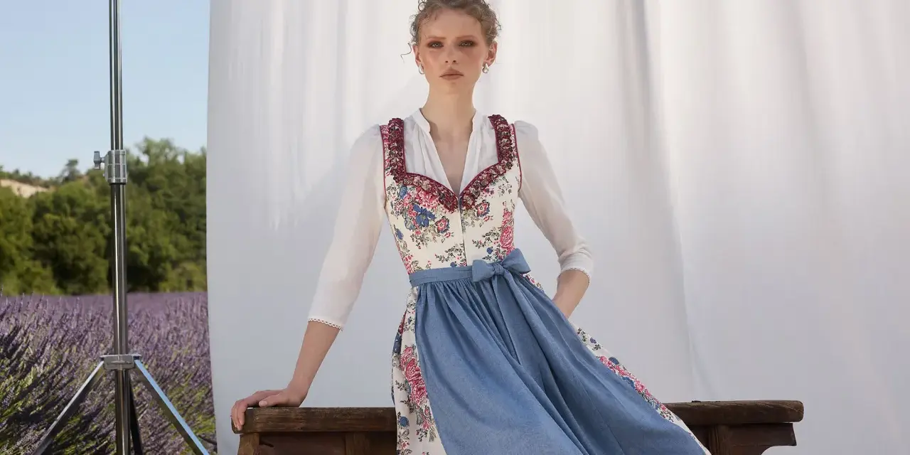 Ein Dirndl im floralen Muster mit blauem Rock, ein moderner Dirndl-Trend, posiert vor Lavendelfeld-Kulisse.