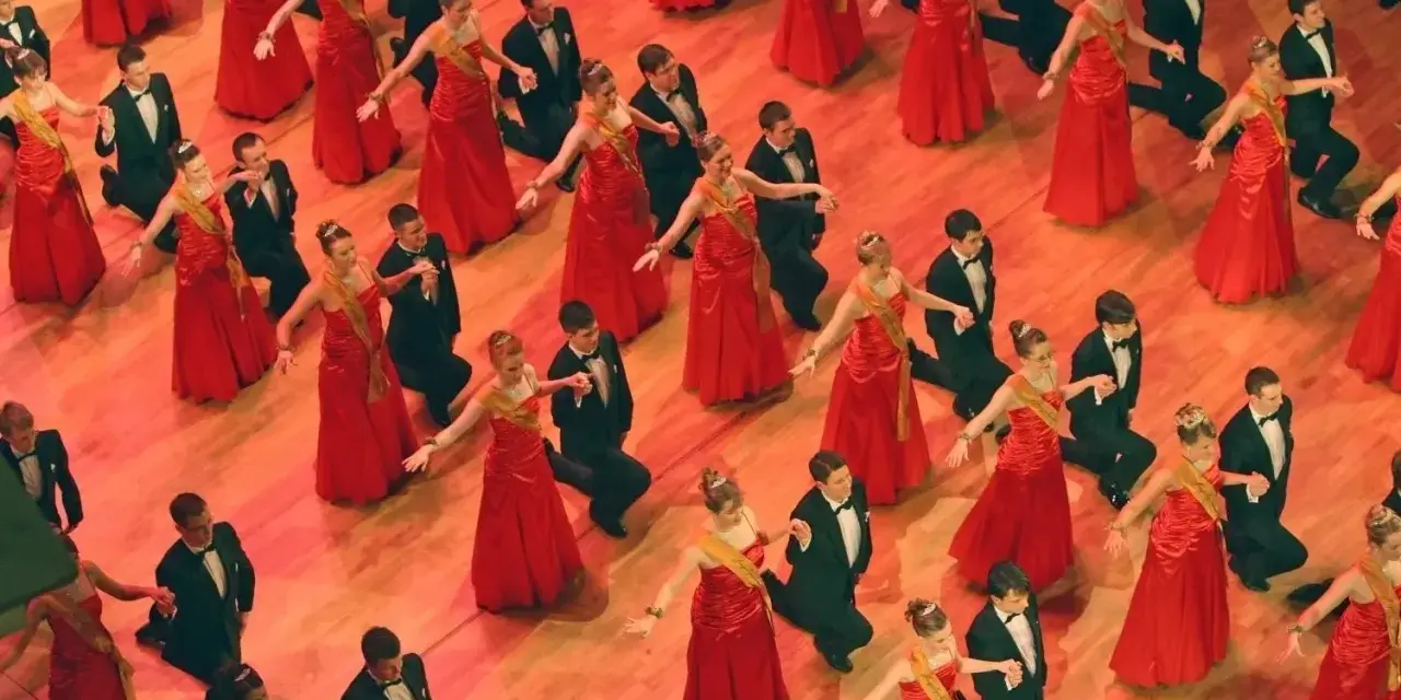 Junge Paare in roten Kleidern und schwarzen Anzügen tanzen. Die Kleiderordnung der Semperoper wird hier elegant umgesetzt.