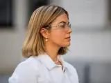 Frau mit einem stylischen **long bob** und auffälligen Sonnenbrillen, trägt eine weiße Jacke und Perlenschmuck.