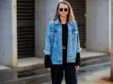 Stylische Frau mit lässiger Jeansjacke kombinieren mit schwarzem Crop-Top und Hose. Sonnenbrille und kleine Tasche runden den Look ab.