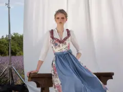 Ein Dirndl im floralen Muster mit blauem Rock, ein moderner Dirndl-Trend, posiert vor Lavendelfeld-Kulisse.