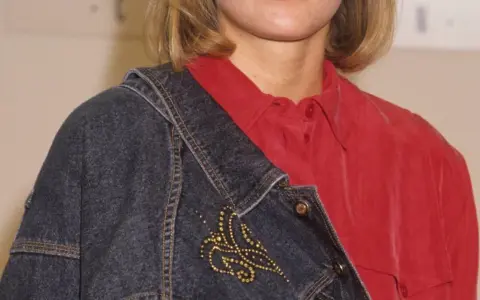 Eine Frau trägt eine rote Bluse und eine blaue Jeansjacke mit einer goldenen Schmetterlingsbrosche.